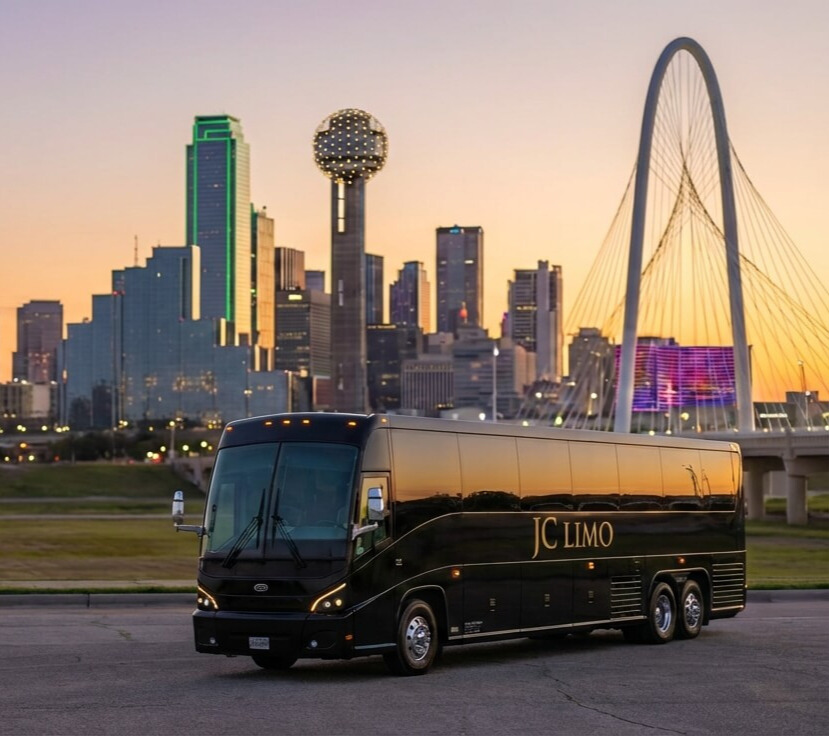 Black JC Limo 56-passenger motor coach parked in front of the Dallas skyline at sunset near Margaret Hunt Hill Bridge, luxury charter bus service in DFW.